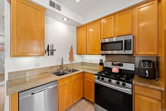 kitchen with light tile patterned floors, light stone countertops, sink, and stainless steel appliances