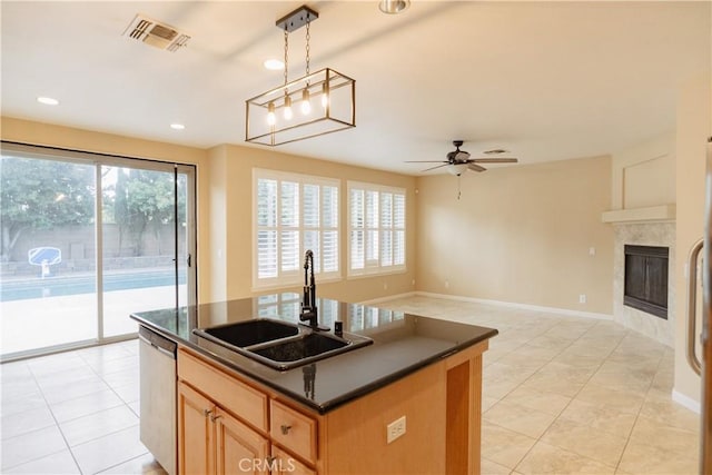 kitchen with sink, decorative light fixtures, stainless steel dishwasher, a fireplace, and a kitchen island with sink