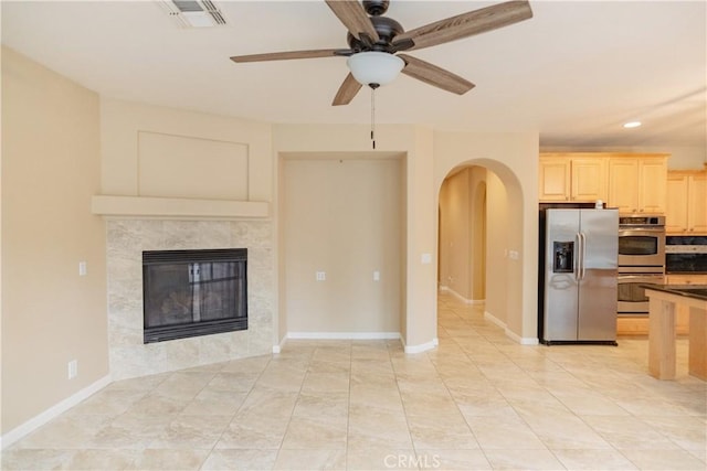 unfurnished living room with a tiled fireplace and ceiling fan