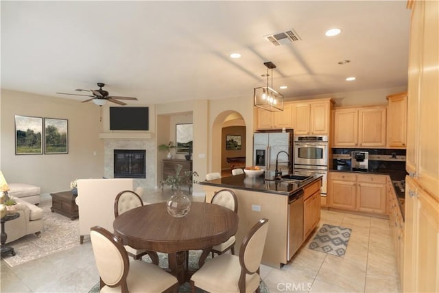 kitchen featuring appliances with stainless steel finishes, pendant lighting, light brown cabinetry, sink, and a center island with sink