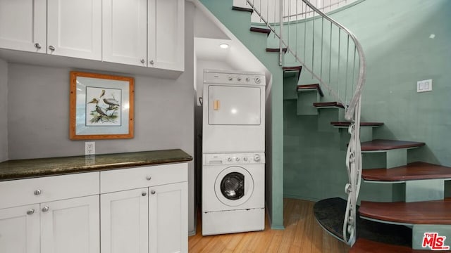 laundry room with cabinets, light hardwood / wood-style flooring, and stacked washing maching and dryer