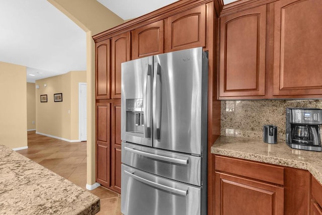 kitchen featuring tasteful backsplash, light tile patterned floors, stainless steel refrigerator with ice dispenser, and light stone counters