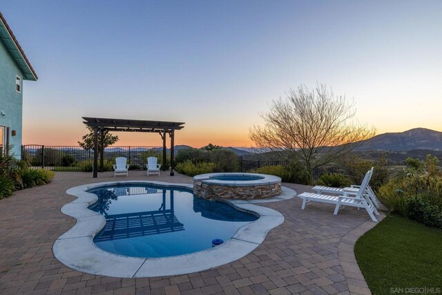 pool at dusk featuring a pergola, a mountain view, a patio, and an in ground hot tub