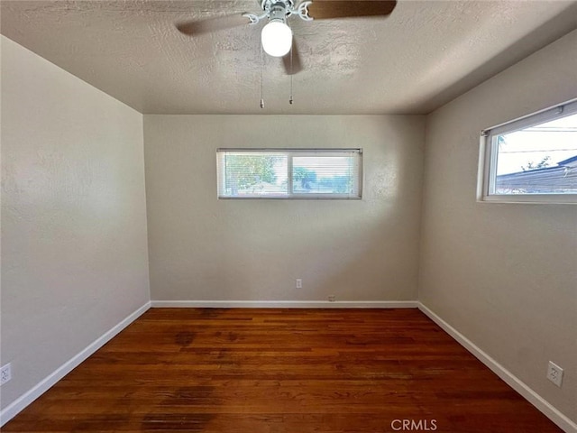 spare room featuring a textured ceiling, dark wood-type flooring, a wealth of natural light, and ceiling fan