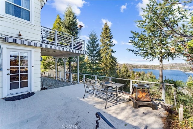 view of patio with a water view, an outdoor fire pit, and a balcony