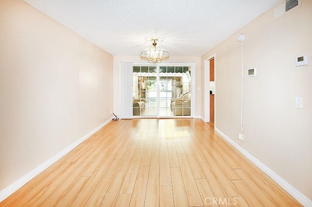 unfurnished room featuring light wood-type flooring, a textured ceiling, and a notable chandelier