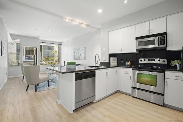 kitchen with appliances with stainless steel finishes, white cabinets, kitchen peninsula, and sink