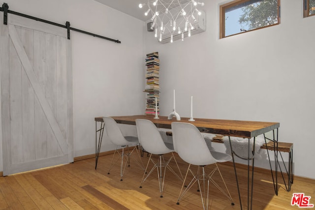 dining room with a chandelier, a barn door, and light hardwood / wood-style flooring