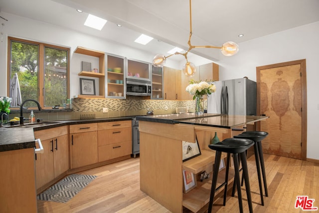 kitchen with a skylight, a kitchen bar, appliances with stainless steel finishes, light brown cabinetry, and a kitchen island