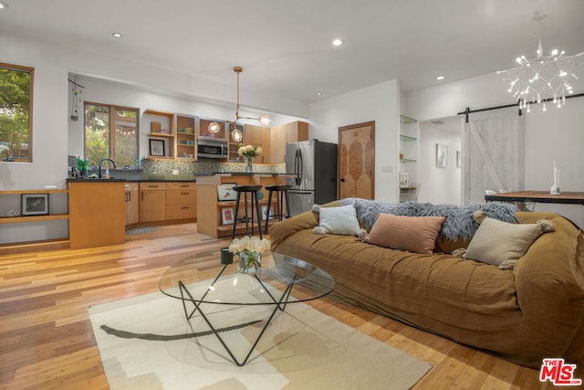 living room with sink, an inviting chandelier, a barn door, and light wood-type flooring