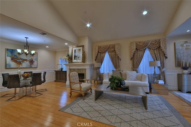 living room with lofted ceiling, a fireplace, an inviting chandelier, and light hardwood / wood-style flooring