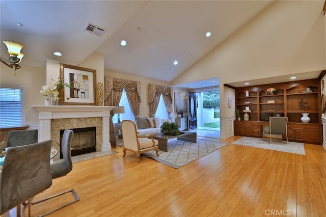 living room with high vaulted ceiling, a healthy amount of sunlight, light wood-type flooring, and a fireplace