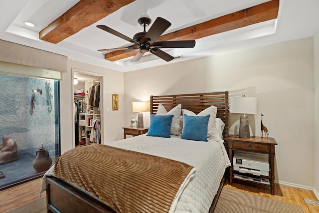 bedroom with hardwood / wood-style floors, a walk in closet, a closet, ceiling fan, and a tray ceiling