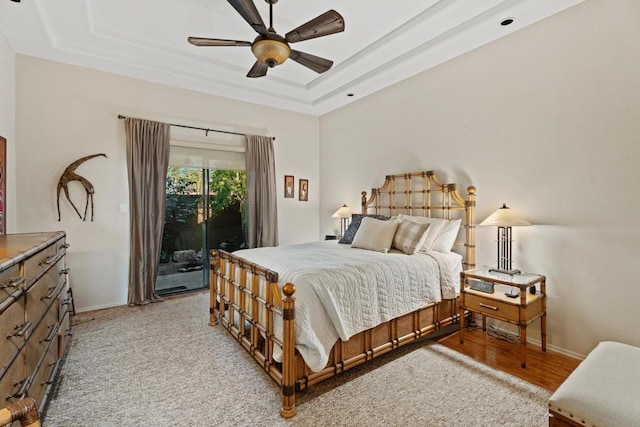 bedroom with ceiling fan, access to exterior, a tray ceiling, and light hardwood / wood-style flooring