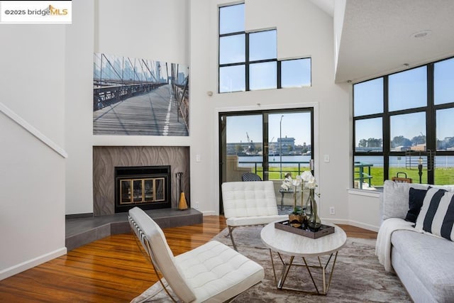 living room featuring a water view, a towering ceiling, a tile fireplace, and hardwood / wood-style floors