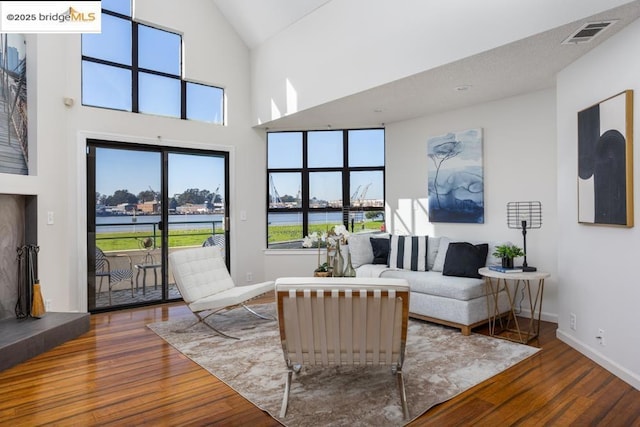 living room featuring a towering ceiling, a water view, and wood-type flooring