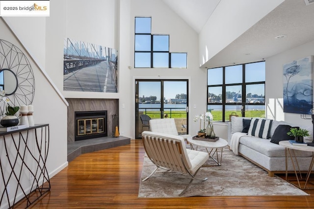 living room featuring a water view, a towering ceiling, a tile fireplace, and hardwood / wood-style flooring