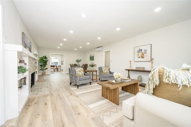 living room with a wall mounted AC, a tiled fireplace, and light wood-type flooring