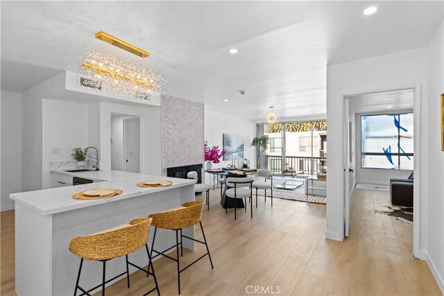 kitchen featuring decorative light fixtures, a fireplace, sink, kitchen peninsula, and light wood-type flooring