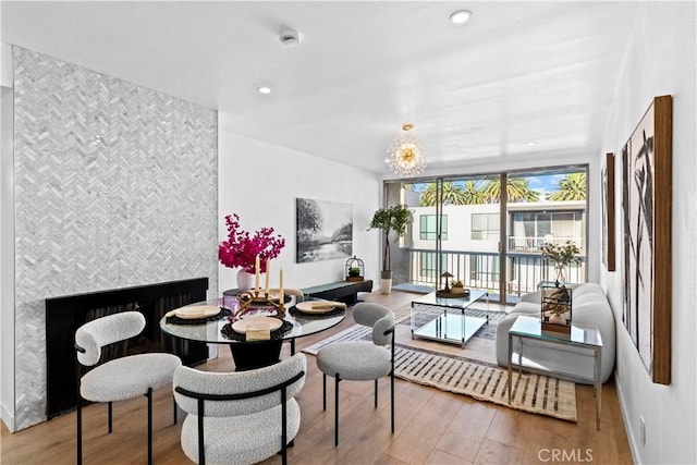 dining area featuring wood-type flooring, a notable chandelier, a tile fireplace, and floor to ceiling windows