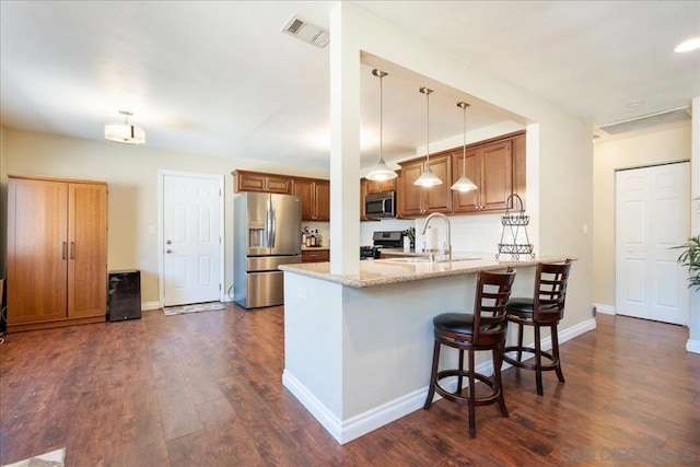 kitchen with appliances with stainless steel finishes, tasteful backsplash, pendant lighting, light stone counters, and sink