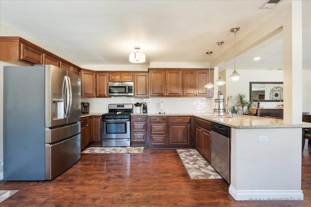 kitchen featuring kitchen peninsula, stainless steel appliances, hanging light fixtures, light stone counters, and sink