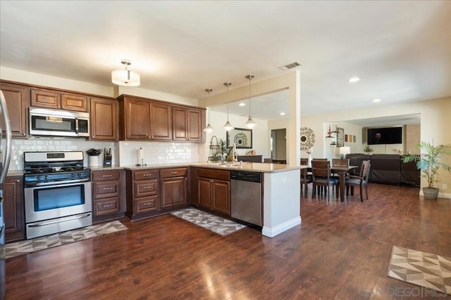 kitchen featuring pendant lighting, stainless steel appliances, sink, backsplash, and kitchen peninsula