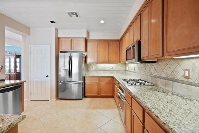 kitchen with light tile patterned floors, decorative backsplash, light stone counters, and stainless steel appliances