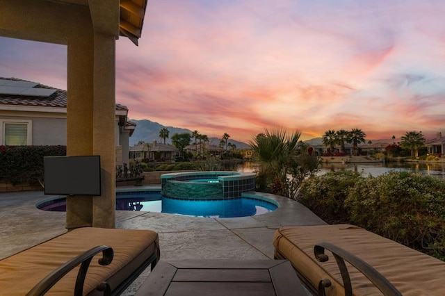 pool at dusk featuring an in ground hot tub and a patio