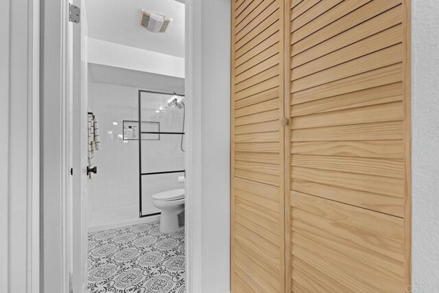 bathroom featuring toilet, tile patterned flooring, and tiled shower