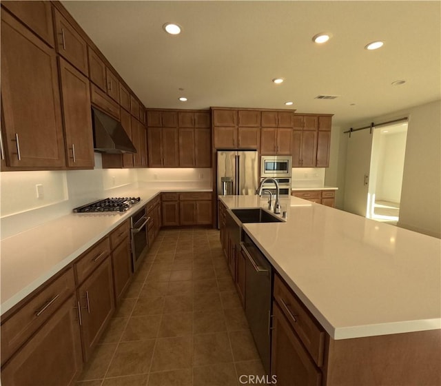 kitchen with a barn door, stainless steel appliances, sink, a large island with sink, and dark tile patterned floors