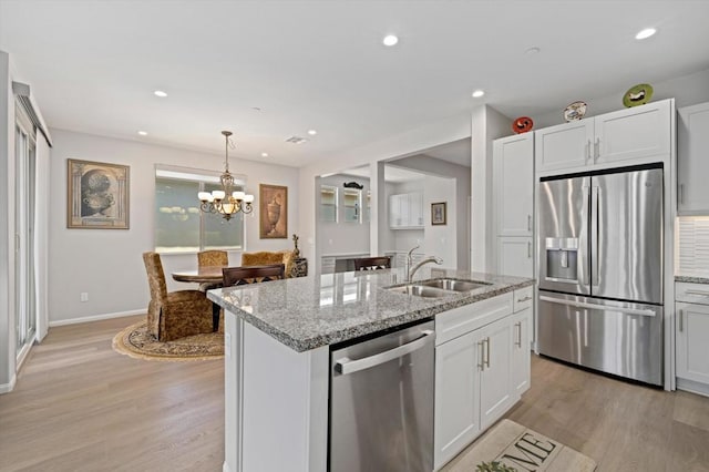 kitchen with white cabinetry, stainless steel appliances, an island with sink, sink, and light stone counters