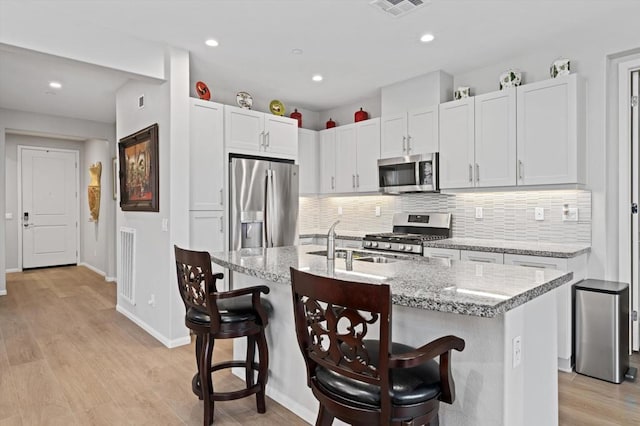 kitchen featuring a breakfast bar area, stainless steel appliances, decorative backsplash, and a kitchen island with sink