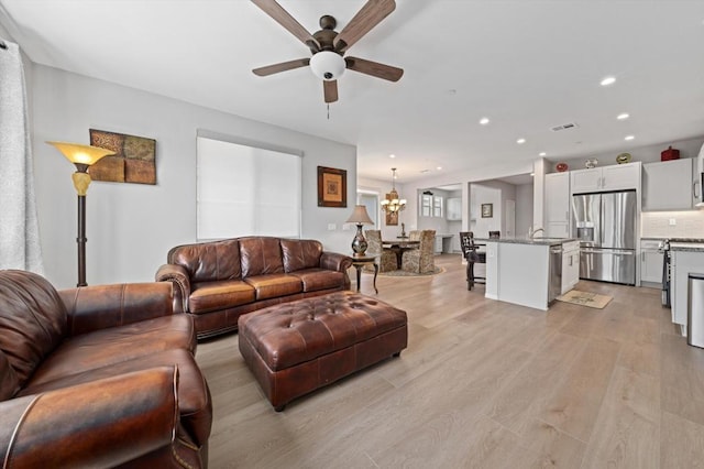 living room featuring light wood-type flooring, ceiling fan with notable chandelier, and sink