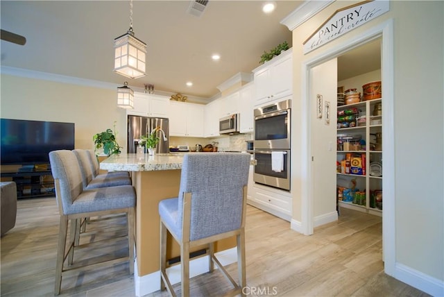 kitchen featuring white cabinets, stainless steel appliances, a kitchen island with sink, light stone counters, and a breakfast bar area