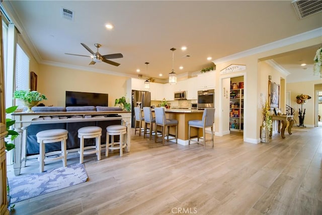 kitchen with white cabinets, appliances with stainless steel finishes, light hardwood / wood-style floors, hanging light fixtures, and a breakfast bar area