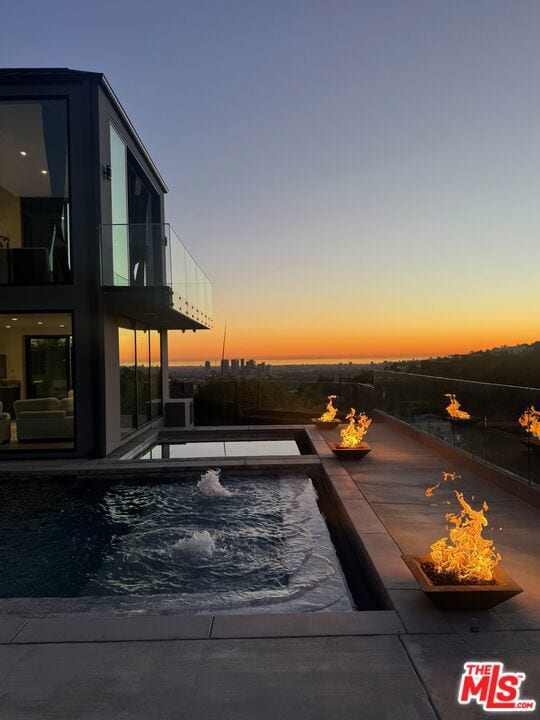 pool at dusk featuring a jacuzzi