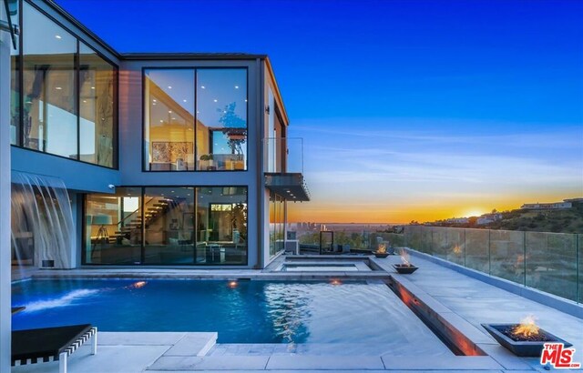 pool at dusk with an outdoor fire pit, a jacuzzi, and a patio area