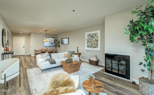 living room with hardwood / wood-style flooring, a textured ceiling, and a stone fireplace