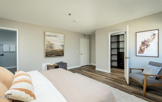 bedroom with a spacious closet, ensuite bathroom, dark hardwood / wood-style floors, a closet, and a textured ceiling