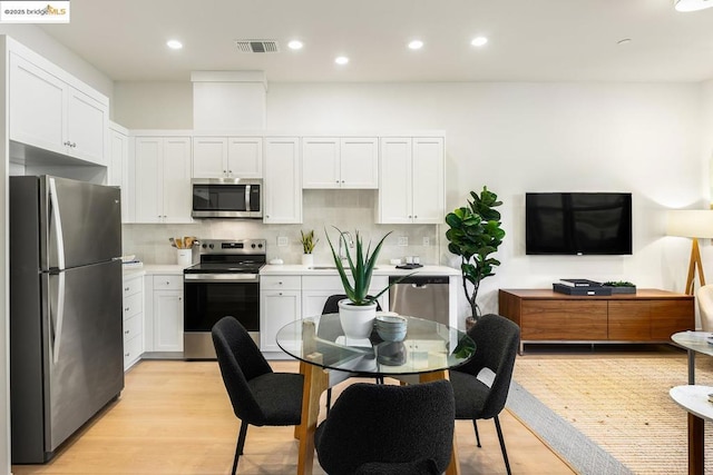 kitchen featuring light wood-type flooring, stainless steel appliances, white cabinetry, and tasteful backsplash