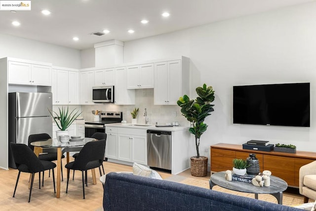 kitchen featuring white cabinetry, stainless steel appliances, decorative backsplash, light hardwood / wood-style flooring, and sink