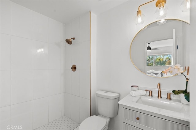 bathroom featuring toilet, ceiling fan, tiled shower, and vanity