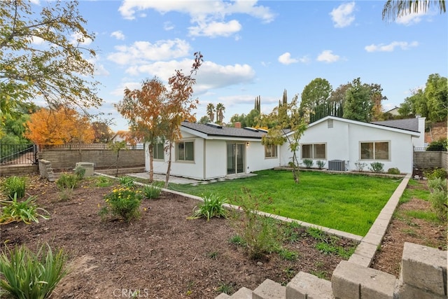 rear view of house featuring cooling unit, a yard, and solar panels