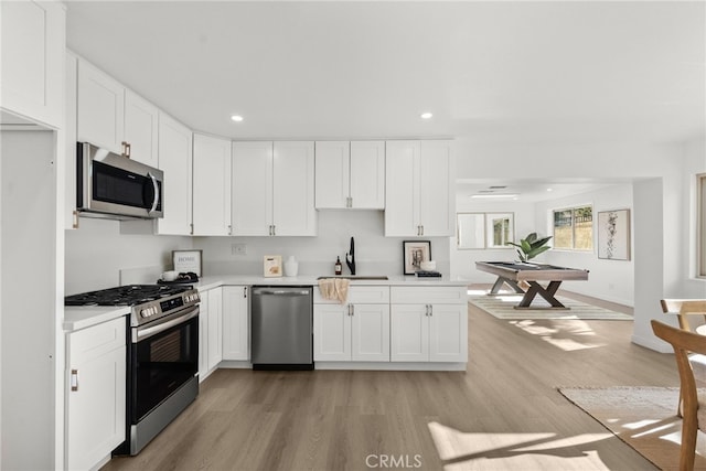 kitchen featuring appliances with stainless steel finishes, white cabinetry, pool table, sink, and light wood-type flooring