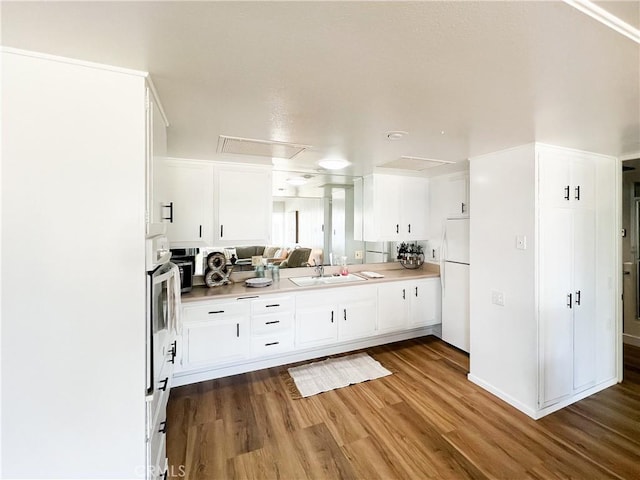 kitchen featuring freestanding refrigerator, white cabinetry, stainless steel oven, a sink, and wood finished floors