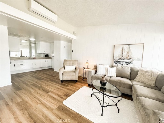 living room featuring light wood-style flooring, a textured ceiling, and a wall mounted AC