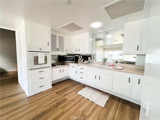 kitchen with white appliances, a sink, visible vents, white cabinetry, and light wood finished floors