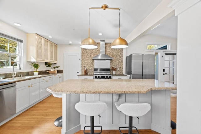 kitchen with pendant lighting, sink, stainless steel appliances, white cabinets, and wall chimney exhaust hood