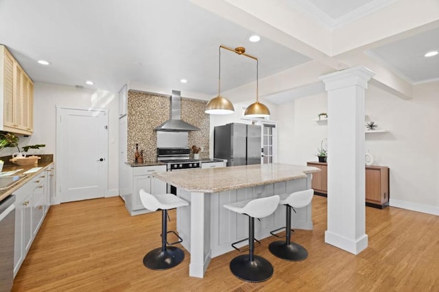 kitchen with wall chimney exhaust hood, decorative light fixtures, a kitchen island, stainless steel appliances, and light hardwood / wood-style floors